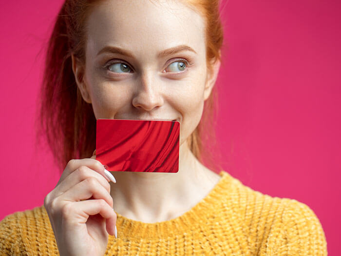 Redhaired beauty female holding credit card isolated over pink wall. Australian Online Shopping Spend